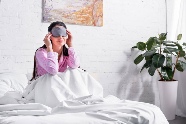 woman in pink pajamas and sleeping mask sitting on bed at home - Photo, Image