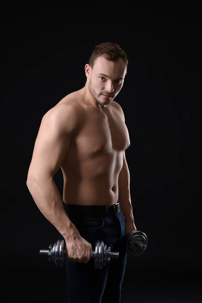 Muscular young bodybuilder with dumb-bells on dark background - Fotoğraf, Görsel