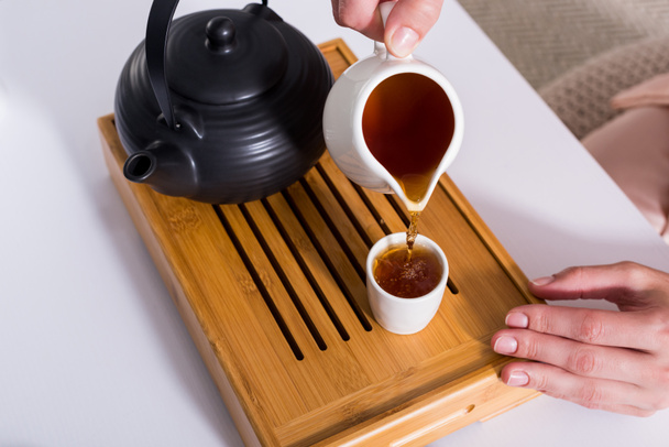 Teilansicht einer Frau, die Tee in Tasse gießt, während sie Teezeremonie zu Hause hat - Foto, Bild