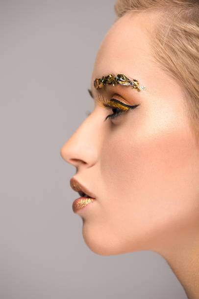 side view of attractive woman with golden glittering makeup isolated on grey - Foto, Bild