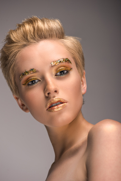 low angle view of attractive woman with golden glitter on face looking at camera isolated on grey - 写真・画像