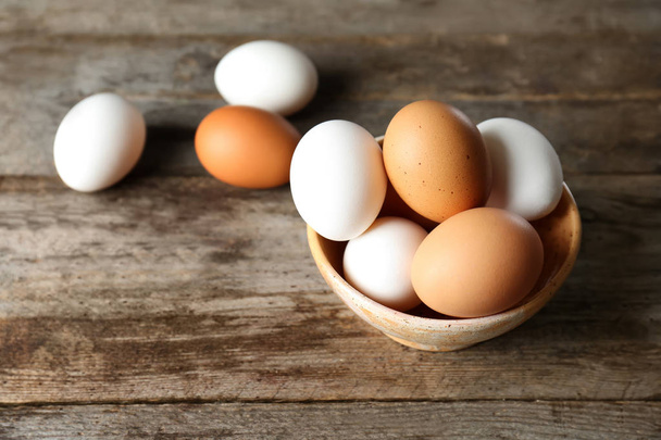 Bowl with chicken eggs on wooden table - Foto, imagen