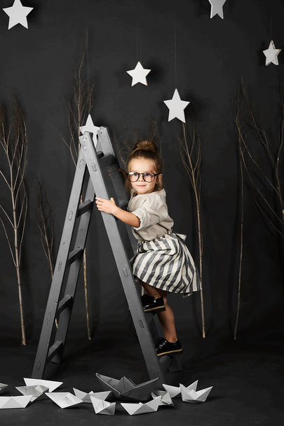 Fanny little girl with glasses on grey background with star and ladder - Foto, Bild