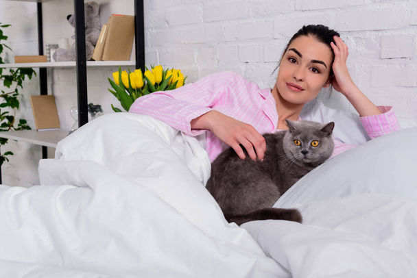 portrait of woman with britain shorthair cat resting in bed at home - Фото, зображення