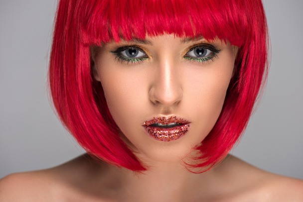 Porträt einer schönen Frau mit roten Haaren und glitzerndem Gesicht, die vereinzelt auf grauem Grund in die Kamera blickt - Foto, Bild