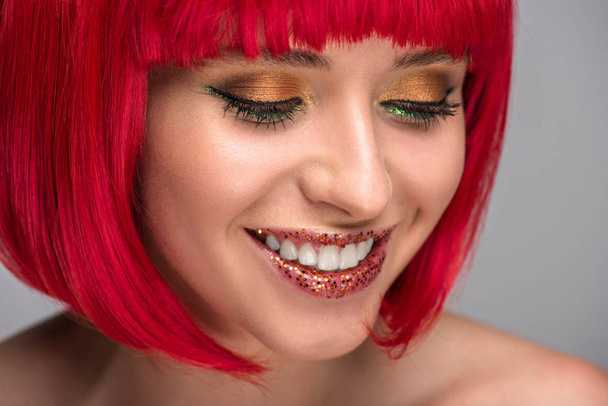 lachende aantrekkelijke vrouw met rood haar en op gezicht geïsoleerd op grijs glitter - Foto, afbeelding