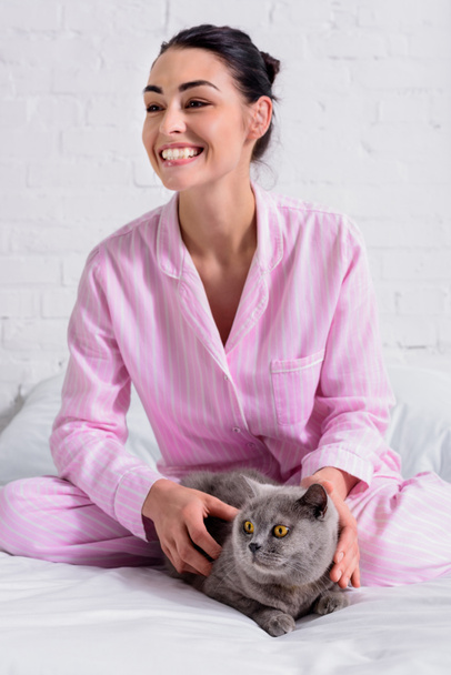 alegre mujer en pijama con britain taquigrafía gato descansando en cama en casa
 - Foto, Imagen