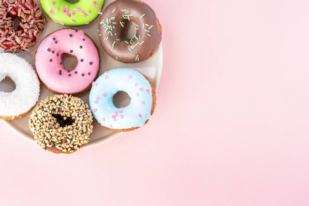 Set of donuts covered with a variety of glaze and sprinkled with sweets on a plate on a pink background - 写真・画像