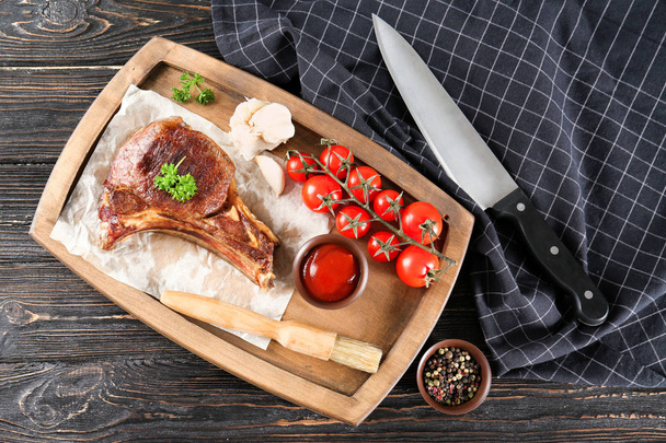 Wooden plate with delicious ribs, tomatoes and sauce on table - Foto, Imagen