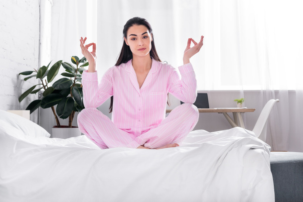 woman in pink pajamas sitting in lotus pose on bed in morning at home - Foto, imagen