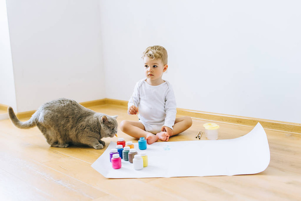 a little blond boy paints a paper with a cat - Фото, изображение