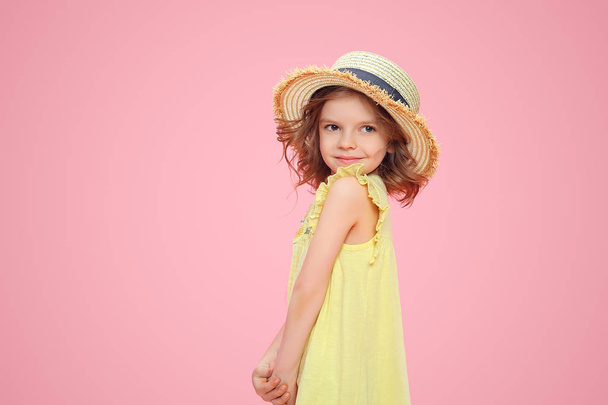 Close up portrait of a Beautiful girl in yellow dress and straw hat. Pretty tenderness kid looking away, posing on a pink studio background. - Foto, afbeelding