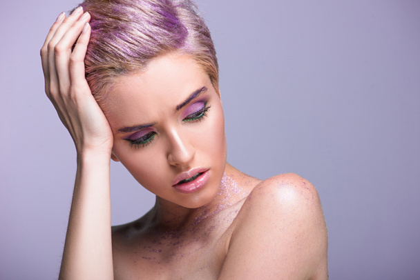 beautiful woman with violet glitter on neck and short hair looking down isolated on violet - Fotografie, Obrázek