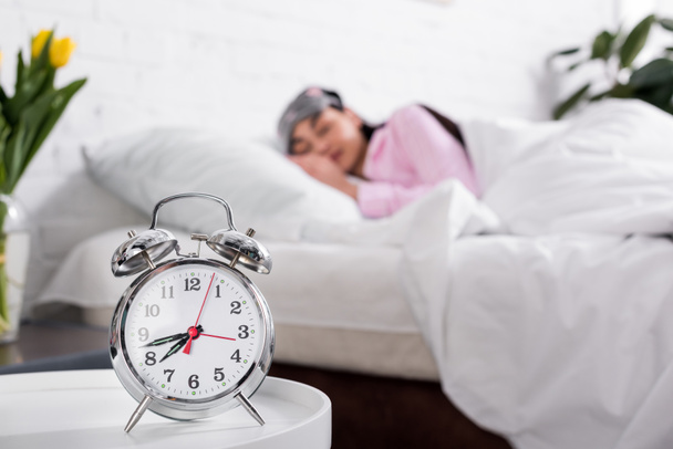 foyer sélectif de l'horloge et la femme en pyjama rose et masque de sommeil dormir dans le lit à la maison
 - Photo, image