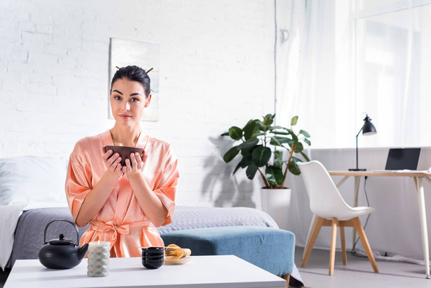 woman in silk bathrobe with wooden bowl in hands having tea ceremony in morning at home - Photo, Image