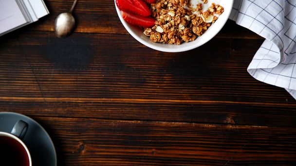  crunchy granola with yoghurt and strawberries in bowl and  with cup of black coffee on wooden table, concept of perfect breakfast - Fotoğraf, Görsel