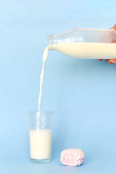 Giet de melk op glas Cup uit transparante glazen fles. In de buurt van roze gebeten marshmallow. - Foto, afbeelding