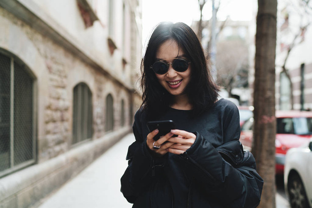 Young asian woman laughing while using smartphone while walking outdoors - Foto, imagen