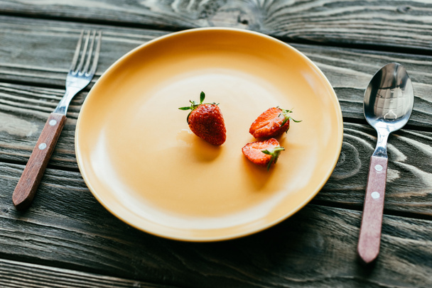 Red strawberries served on plate with spoon and fork on wooden table - Foto, Imagem
