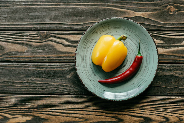 Yellow bell and red chili pepper in plate on wooden table - Foto, imagen