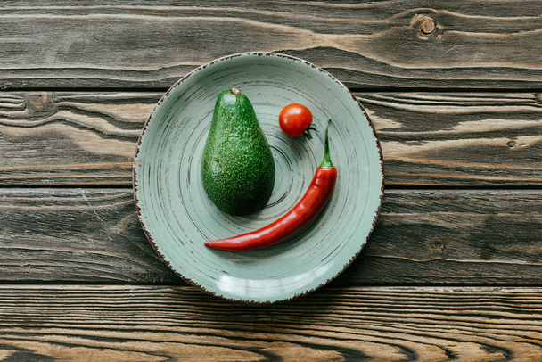 Перец чили с авокадо и помидорами черри в тарелке на деревянном столе
 - Фото, изображение