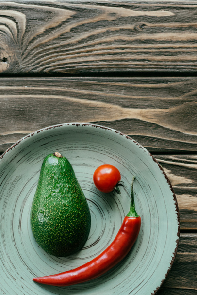 Plate with red vegetables and avocado on wooden table - 写真・画像