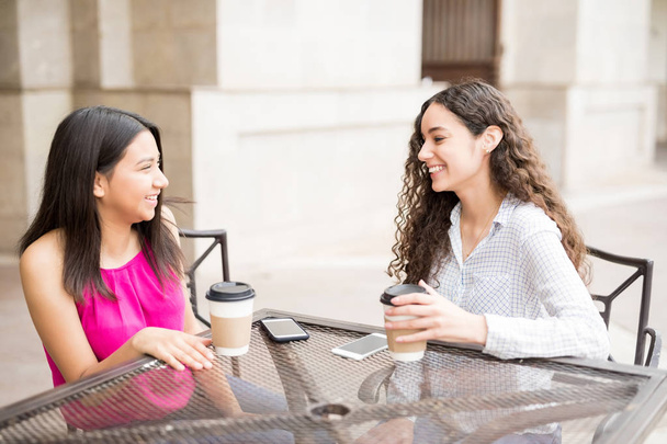 Dos amigas adolescentes pasando el rato en la cafetería al aire libre, charlando mientras toman café
. - Foto, Imagen