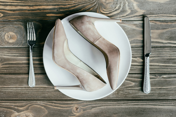 Female heel shoes on plate with cutlery on wooden table - Photo, Image