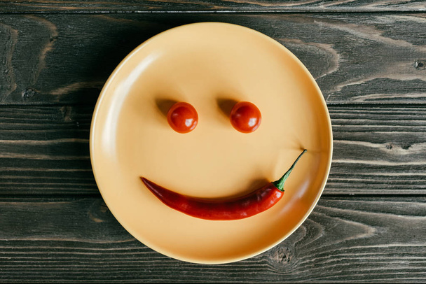 Plate with smile made of pepper and tomatoes on wooden table - Valokuva, kuva