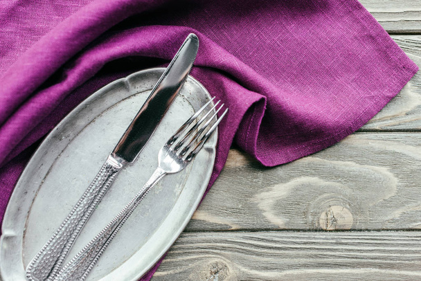 Серебряный поднос с столовыми приборами на фиолетовой салфетке
 - Фото, изображение