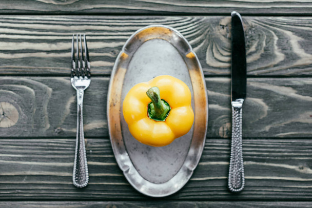 Yellow bell pepper served on plate with knife and fork on wooden table - Fotó, kép