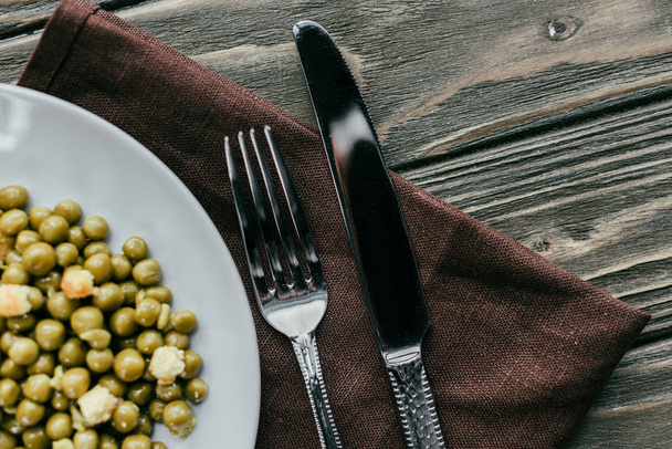 Gabel und Messer auf Teller mit Erbsen auf Textilserviette - Foto, Bild