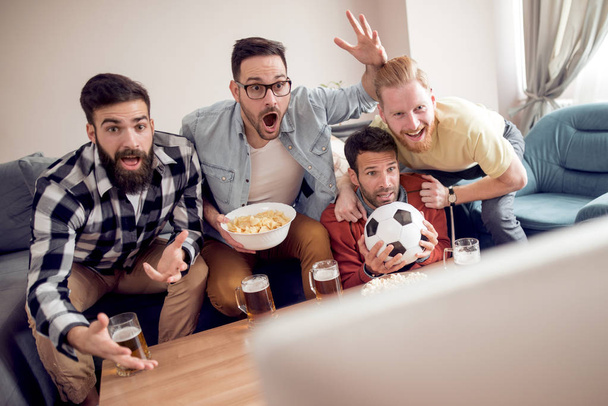 Grupa przyjaciół, oglądając mecz piłki nożnej w telewizji, jedzenia przekąski i picie piwa - Zdjęcie, obraz