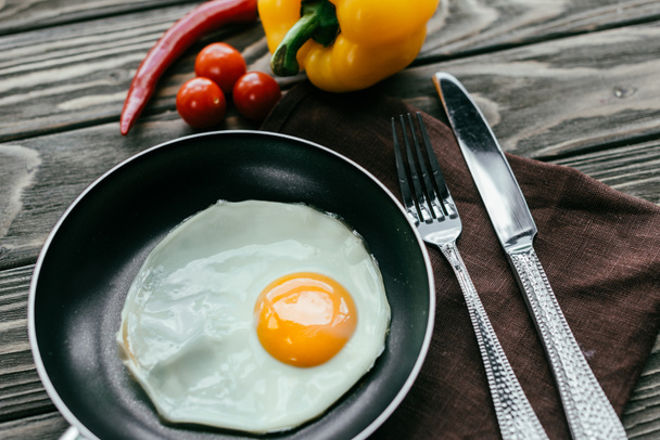 Pan with fried egg on textile napkin with silverware and vegetables - Photo, Image