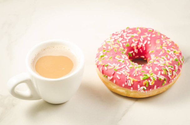 white cup with fresh sugary pink donut/Coffee break white cup with fresh sugary pink donut on a white marble background. - Photo, Image