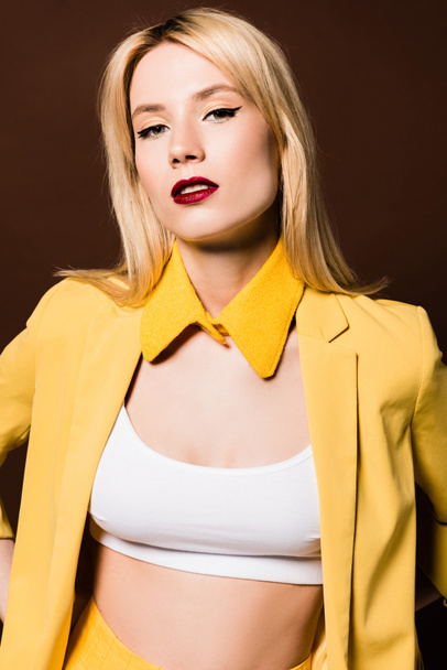 portrait of beautiful blonde girl in fashionable yellow clothes looking at camera isolated on brown - Foto, Bild