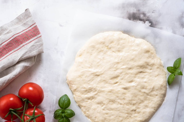 Dough for pizza or focaccia with ingredients, tomatoes, basil, olive oil. Top view. - Foto, Imagen