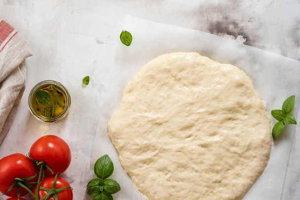 Dough for pizza or focaccia with ingredients, tomatoes, basil, olive oil. Top view. - Foto, Imagem
