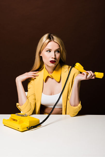 attractive blonde girl holding yellow handset and looking away on brown - Photo, Image