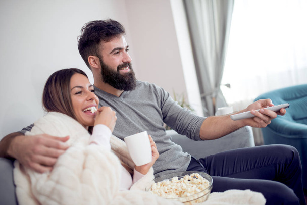 Couple watching tv and eating popcorn at home - Foto, afbeelding