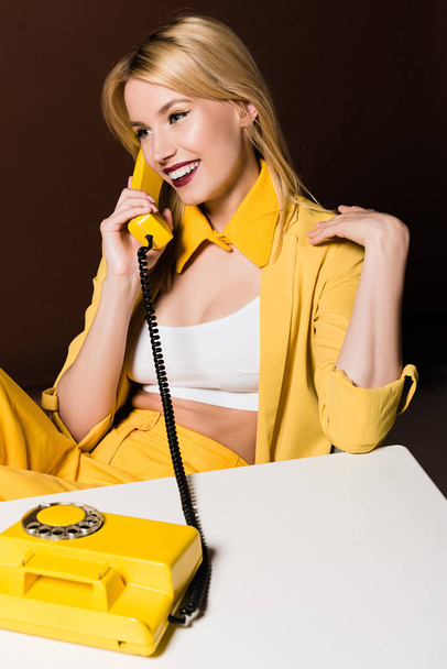 beautiful smiling stylish blonde girl talking by yellow vintage phone on brown - 写真・画像
