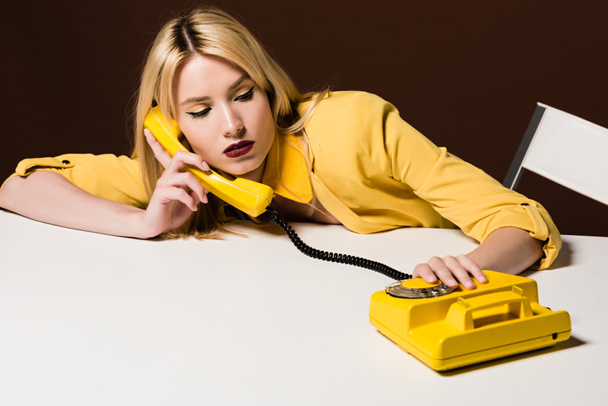 beautiful young woman talking by yellow rotary phone on brown  - Photo, Image