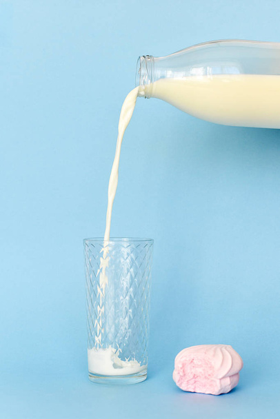 Giet de melk op glas Cup uit transparante glazen fles. In de buurt van roze gebeten marshmallow. - Foto, afbeelding