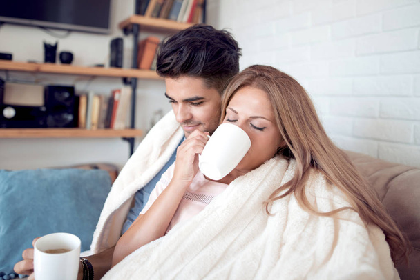 νεαρό ζευγάρι χαλαρώνοντας και πίνοντας τον καφέ στο σπίτι - Φωτογραφία, εικόνα
