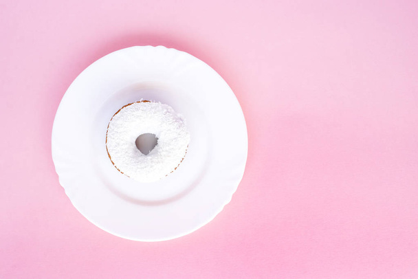 Donut covered with white glaze and sprinkled with coconut shavings on white plate on pink background - Foto, Bild