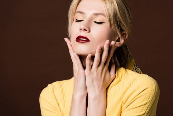 portrait of seductive young blonde woman touching face with hands isolated on brown - Photo, Image