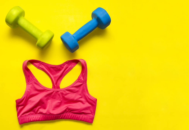 2 dumbbells and a red sports tank top on a yellow background, sports clothing top view, flat lay - Photo, image