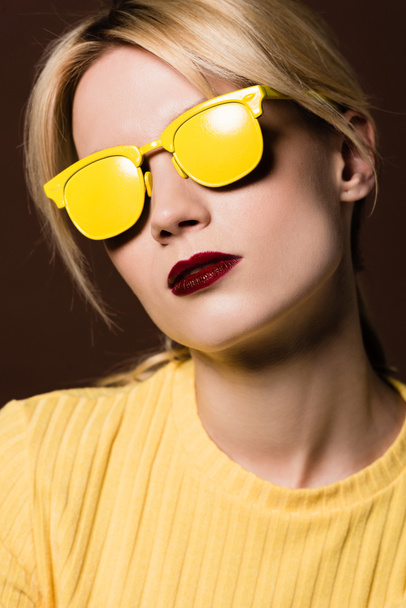 close-up portrait of beautiful blonde girl wearing yellow sunglasses isolated on brown  - Photo, Image