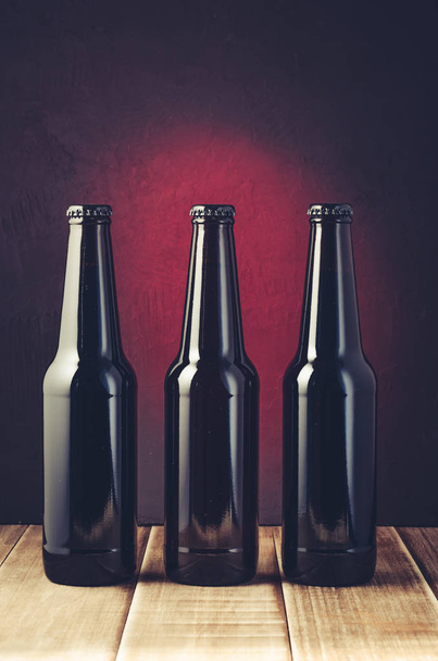 botella negra de cerveza sobre un fondo rojo de un estante de madera / botella negra de cerveza sobre un fondo rojo de un estante de madera. Enfoque tónico y selectivo
 - Foto, Imagen