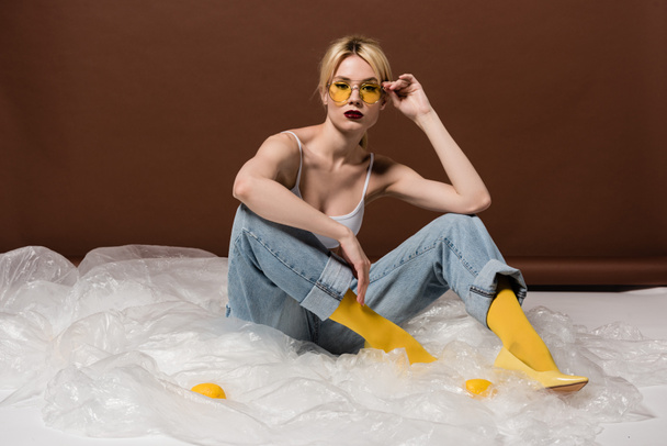 beautiful stylish young blonde woman in yellow sunglasses sitting and looking at camera in studio  - Fotó, kép